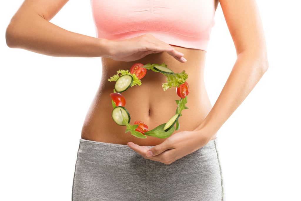 Fit, young woman holding a circle made out of vegetables over her abdomen