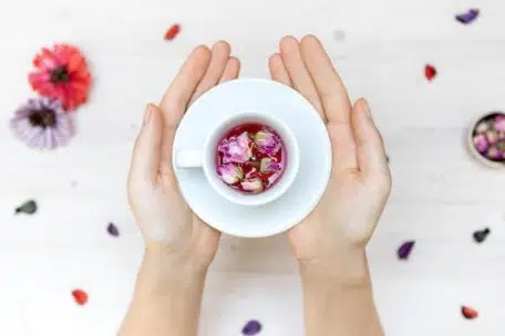 high angle shot of a person holding a white teacup with rose petals on a blurred background